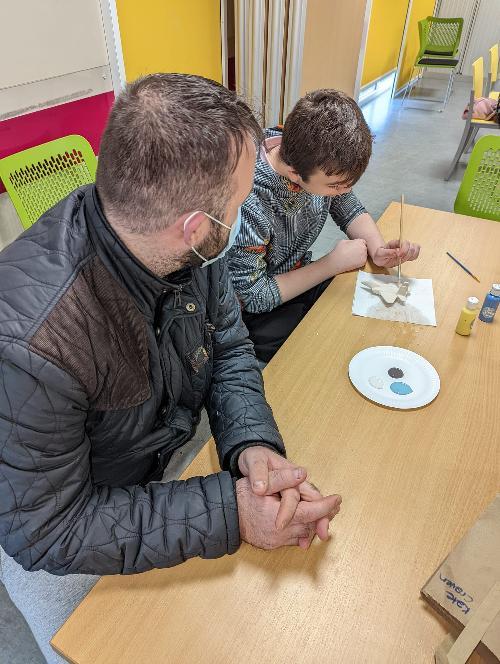 Young boy painting a pottery plan while dad watches